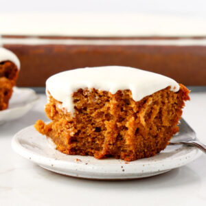 Slice of pumpkin cake topped with frosting on a white plate with a fork.