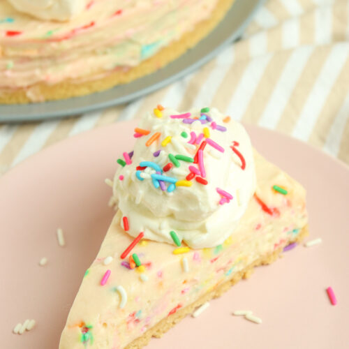 slice of No-Bake Birthday Cake Cheesecake topped with whipped cream and sprinkles