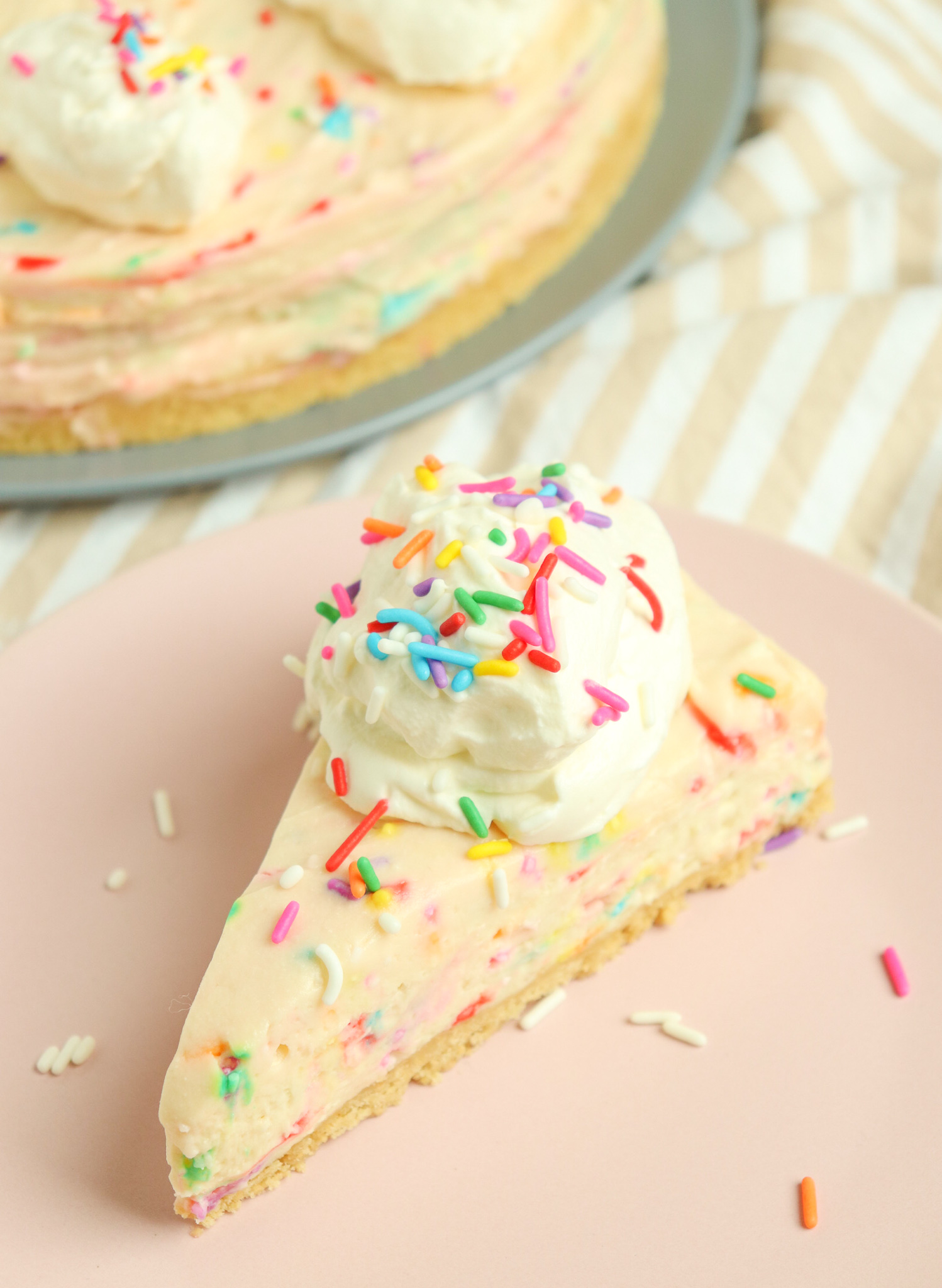 slice of No-Bake Birthday Cake Cheesecake topped with whipped cream and sprinkles