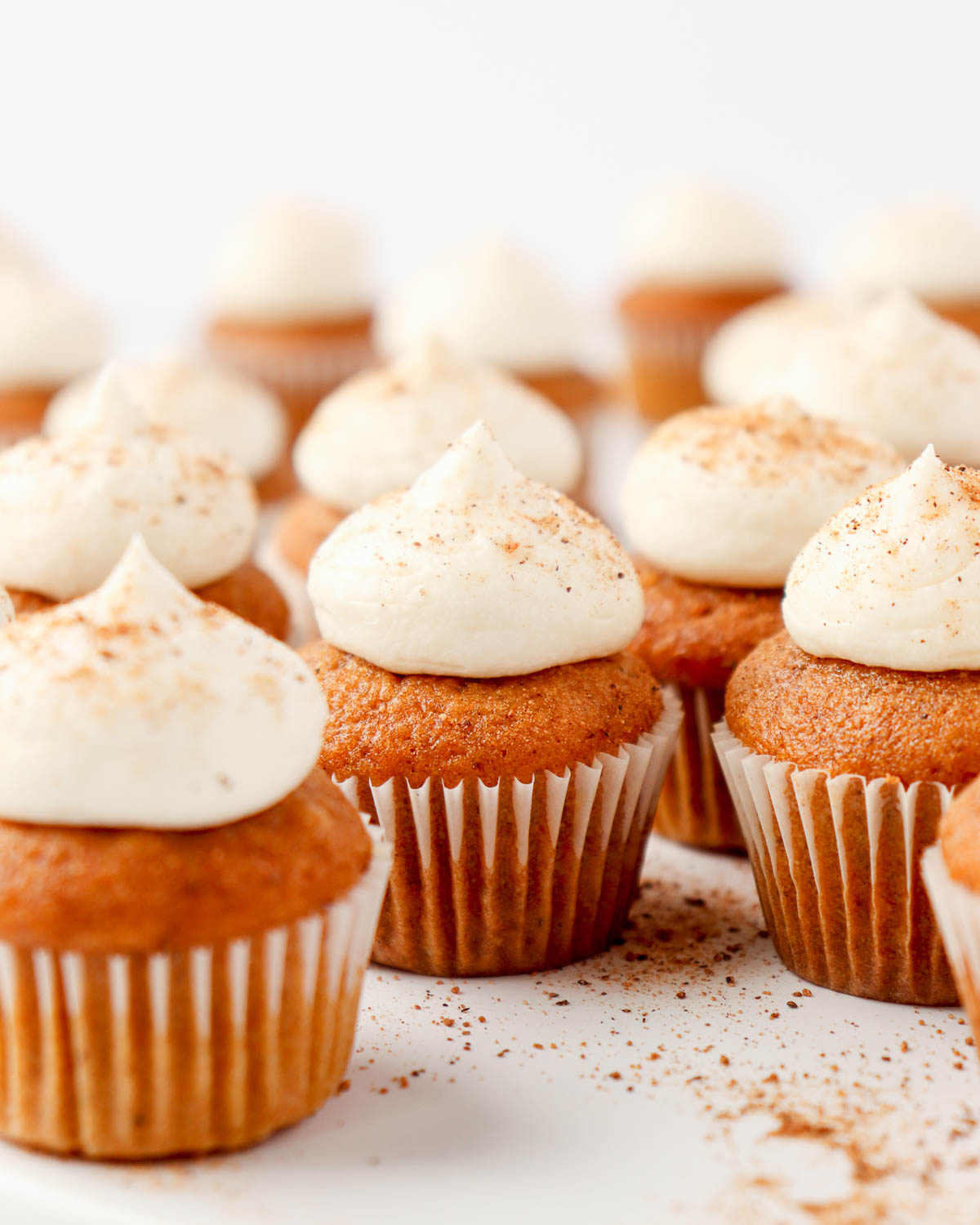 Mini pumpkin cupcakes topped with cream cheese frosting and a sprinkle of nutmeg on a white plate.