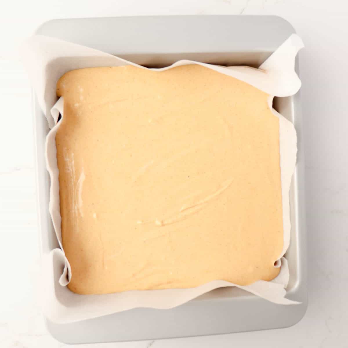 Cheesecake batter in a metal pan lined with parchment paper on top of the gingersnap crust.