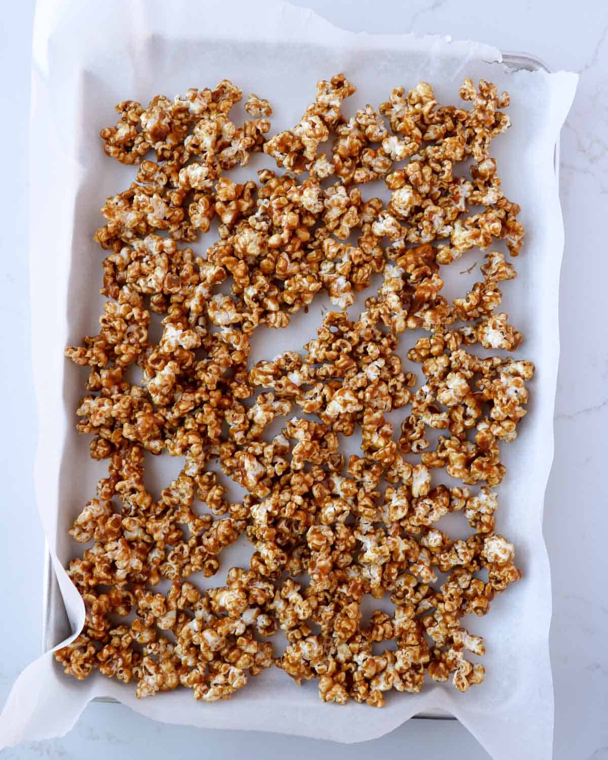 Unbaked caramel corn spread out on a baking sheet lined with parchment paper.