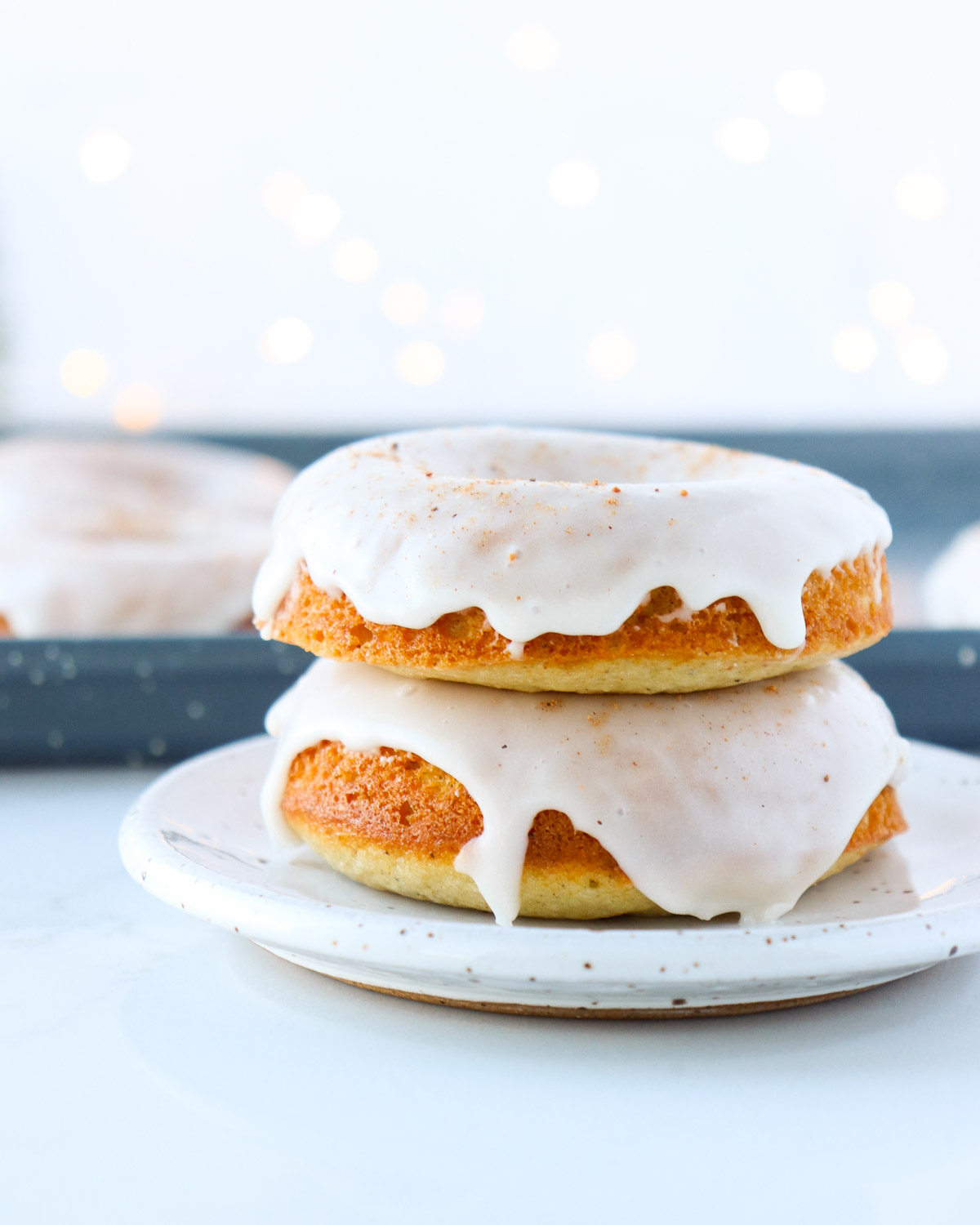 Two donuts with glaze on top stacked on a white plate.