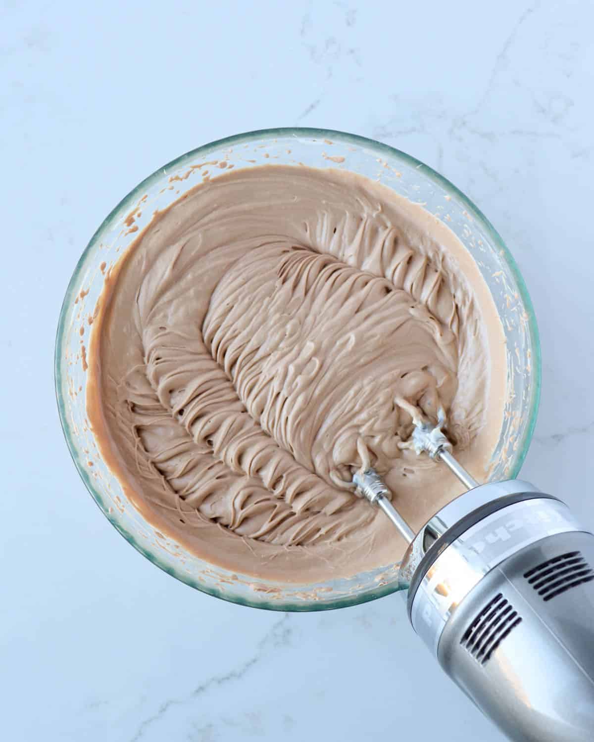 Smooth whipped chocolate mint cheesecake batter in a bowl with an electric handheld mixer.