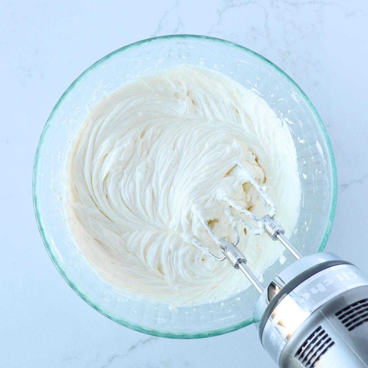 Softened cream cheese, powdered sugar, peppermint extract, and vanilla whipped together in a glass mixing bowl with an electric handheld mixer.