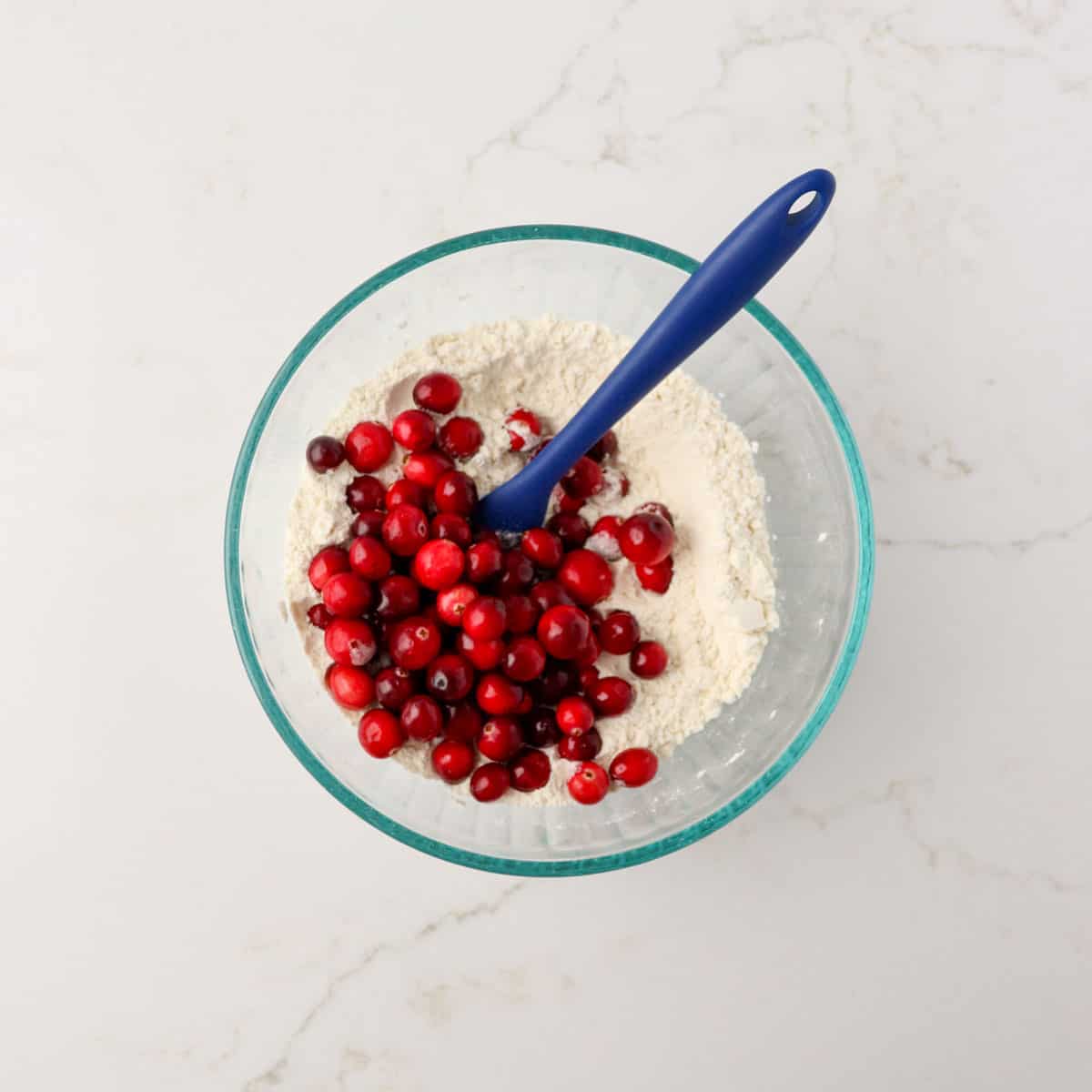 Flour, baking soda, and baking powder combined in a bowl with fresh cranberries added.