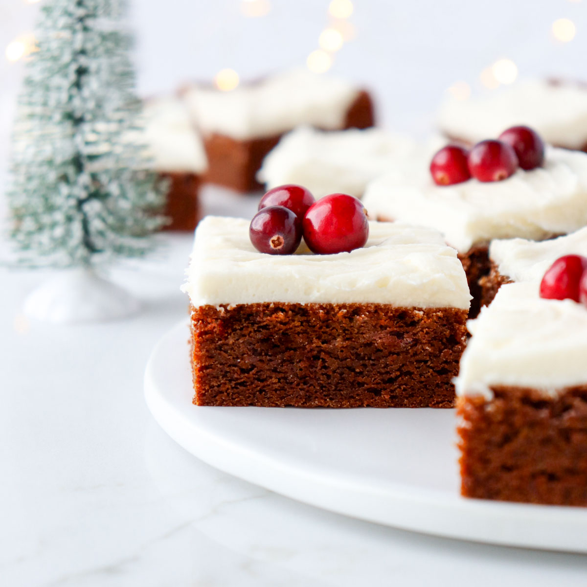 Ginger molasses cookie bar topped with cream cheese frosting and fresh cranberries as a garnish.