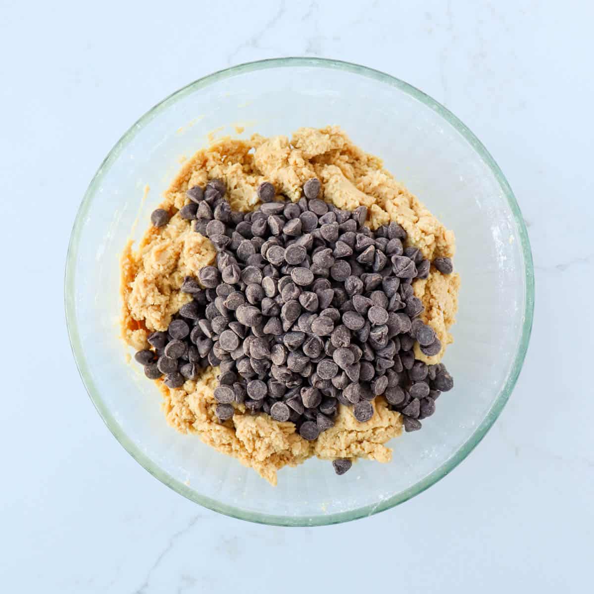 Chocolate chips added to cookie dough in a bowl.