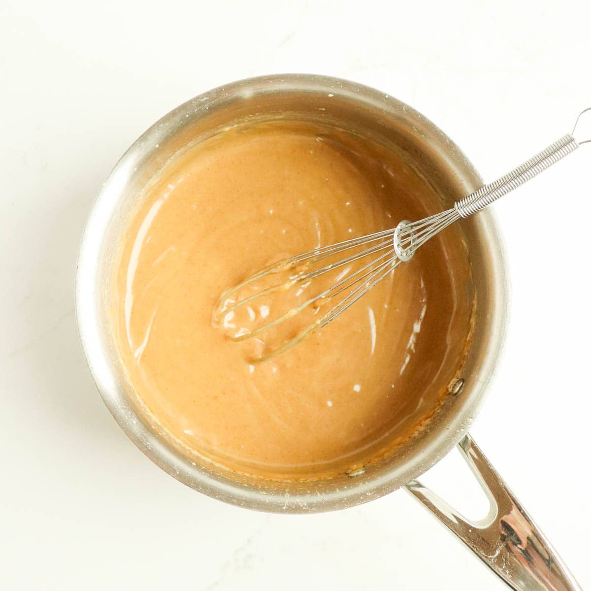 Cooked caramel in a pot with a whisk.