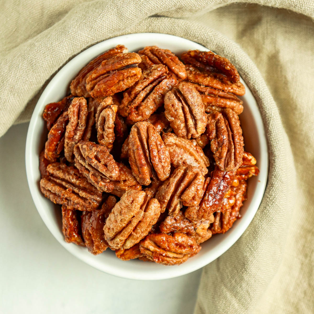 Bowl of candied pecans with a beige towel wrapped around it.