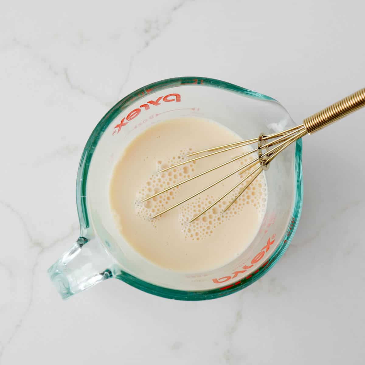 Milk, egg, and vanilla combined in a glass measuring cup.