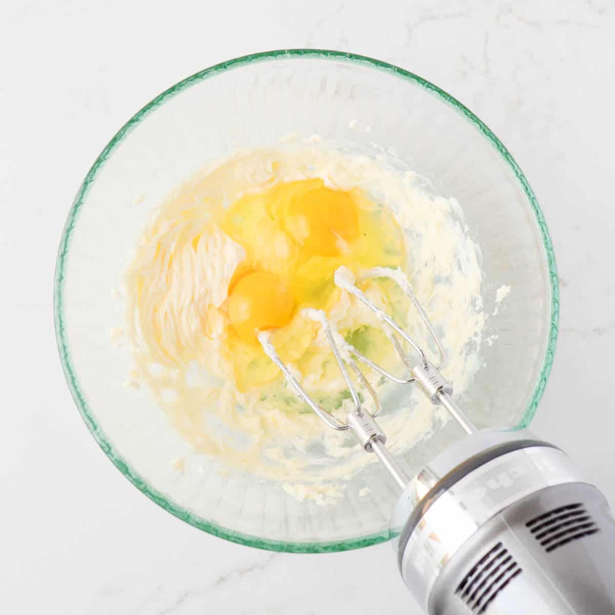 Creamed butter with eggs added in a mixing bowl.