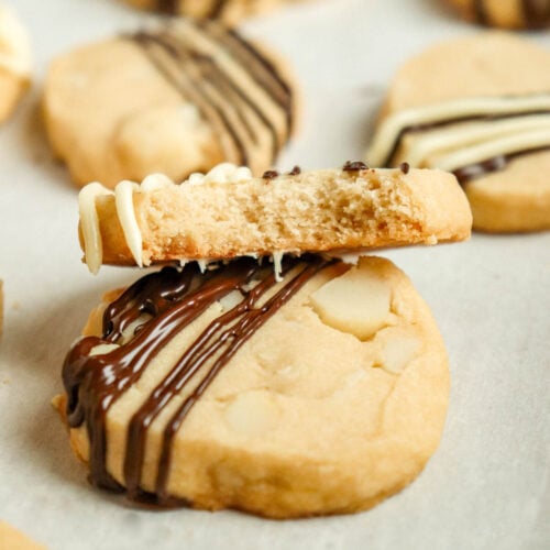 Macadamia shortbread cookie topped with melted chocolate with a bite taken out of it.