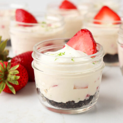 Jar cheesecakes topped with lime zest and slices of strawberries.