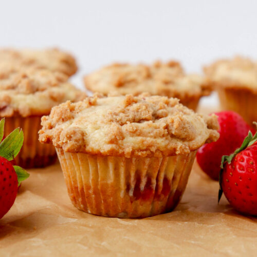 Muffin topped with streusel topping surrounded by fresh strawberries.