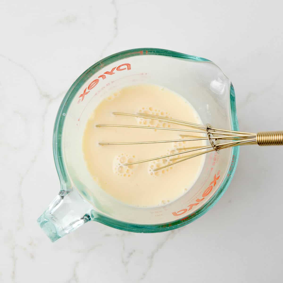 Milk and egg whisked together in a glass measuring cup.