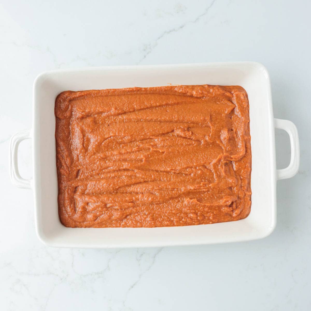 Pumpkin filling in the bottom of a white baking dish.