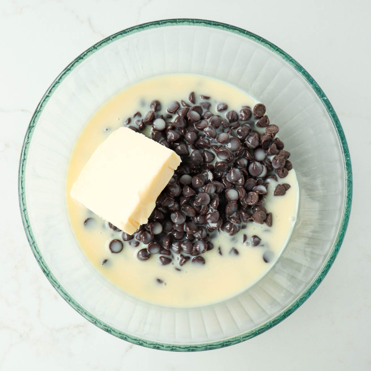 Sweetened condensed milk, chocolate chips, and butter in a glass mixing bowl.