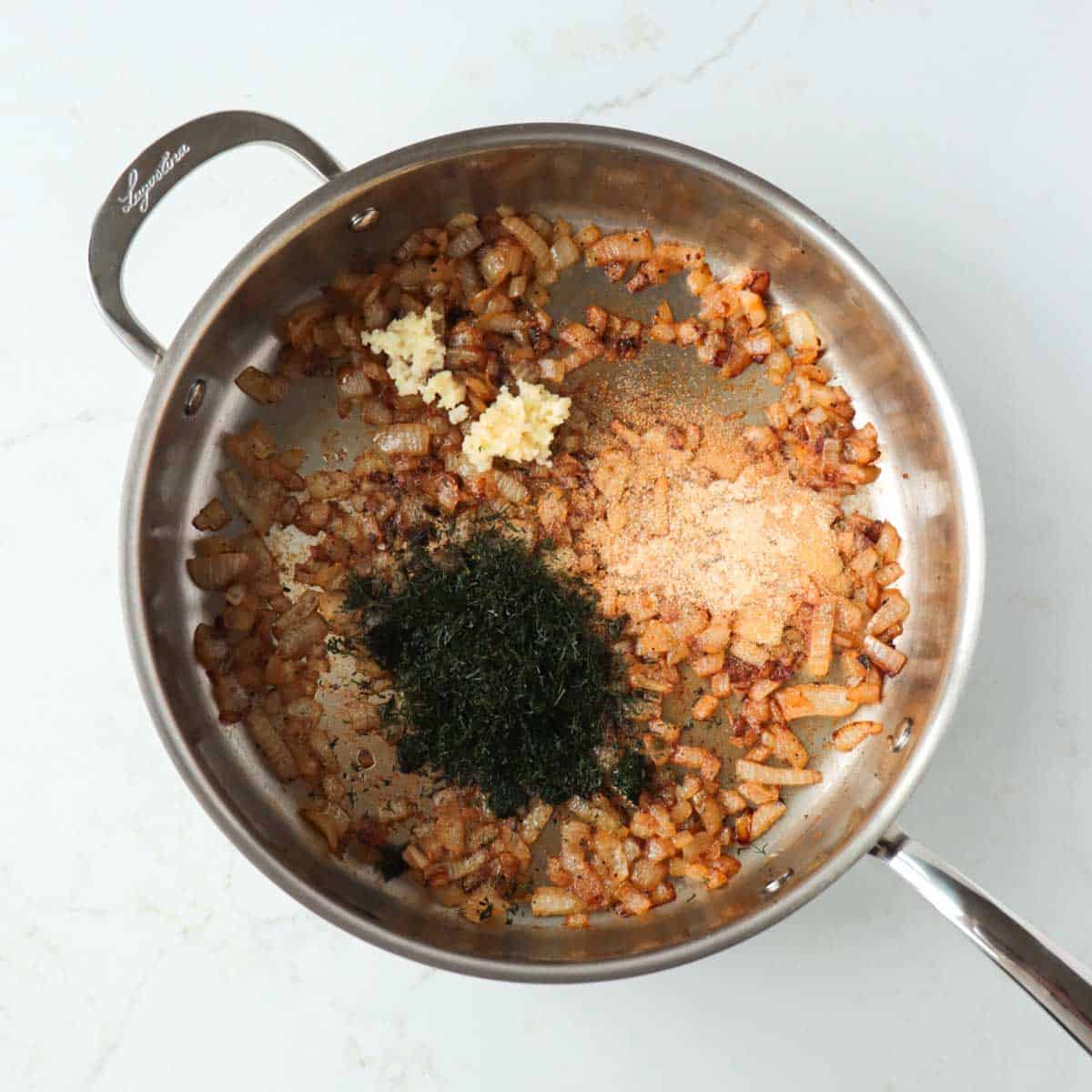 Dill, garlic, and onion powder added to caramelizing onions in a pan.