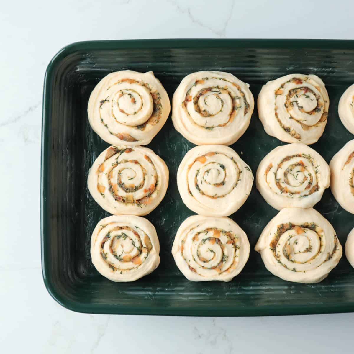 Rolls in dark green baking pan before rising.