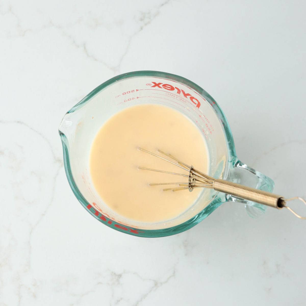 Wet ingredients whisked together in a glass measuring cup.