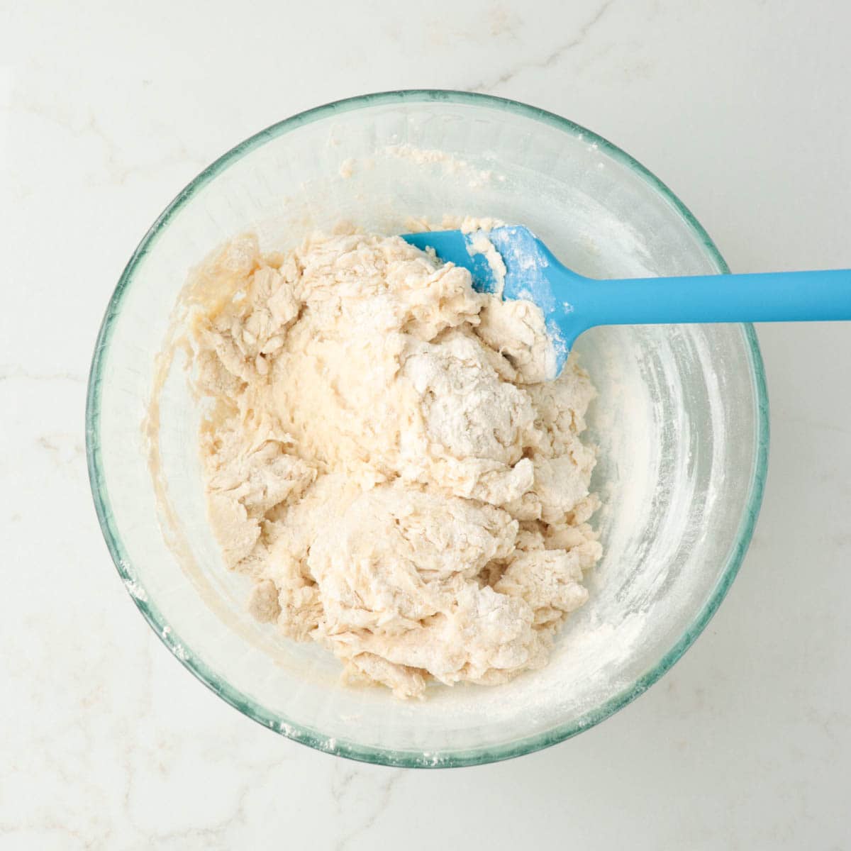 Dough beginning to come together in a mixing bowl.