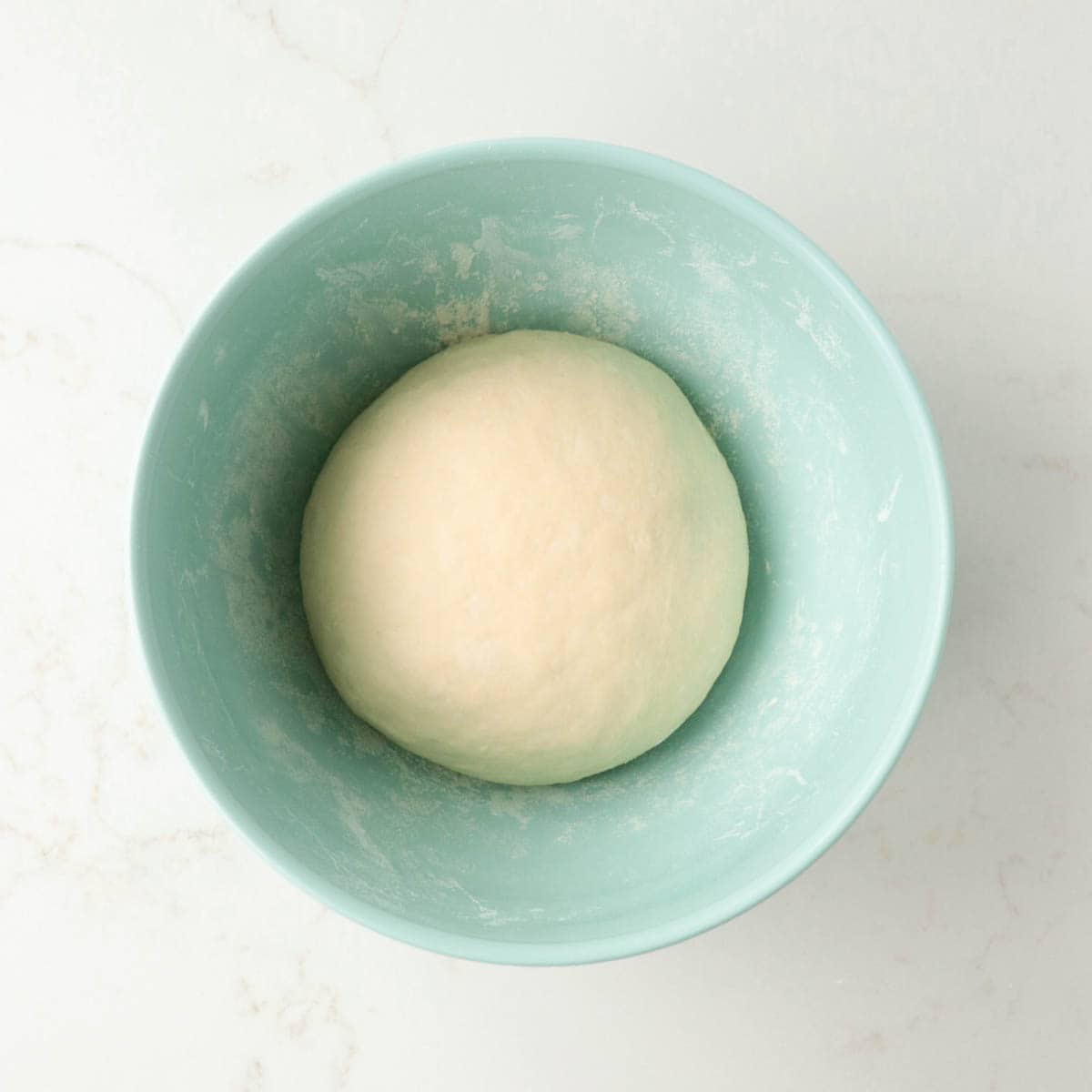 Kneaded dough in a blue bowl before rising.