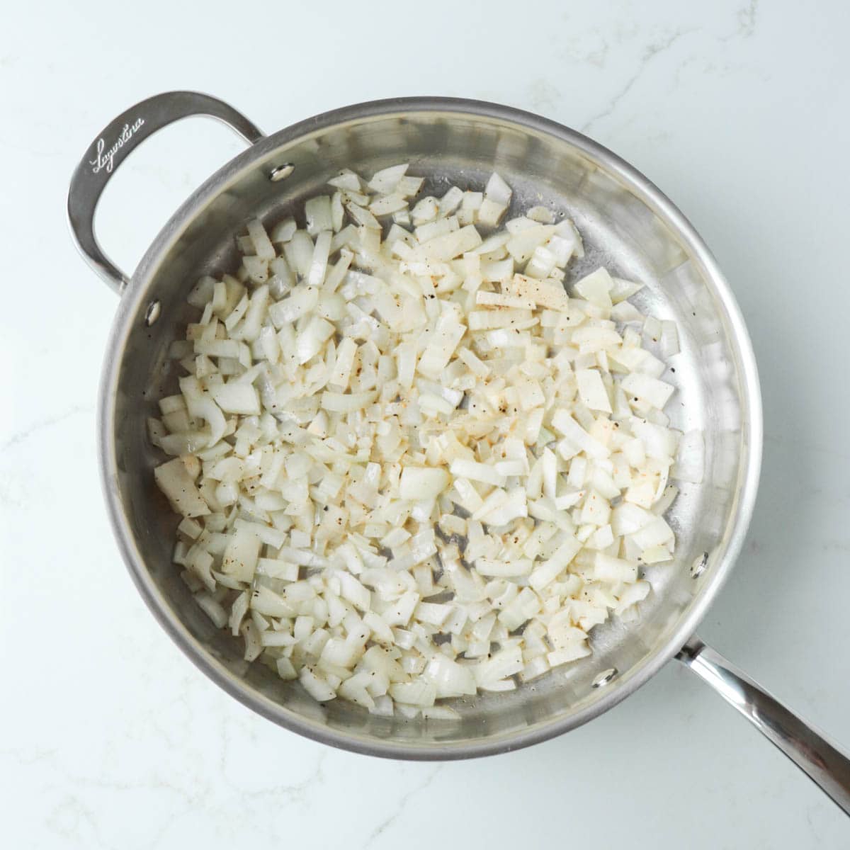 Chopped white onions in a metal pan with butter.