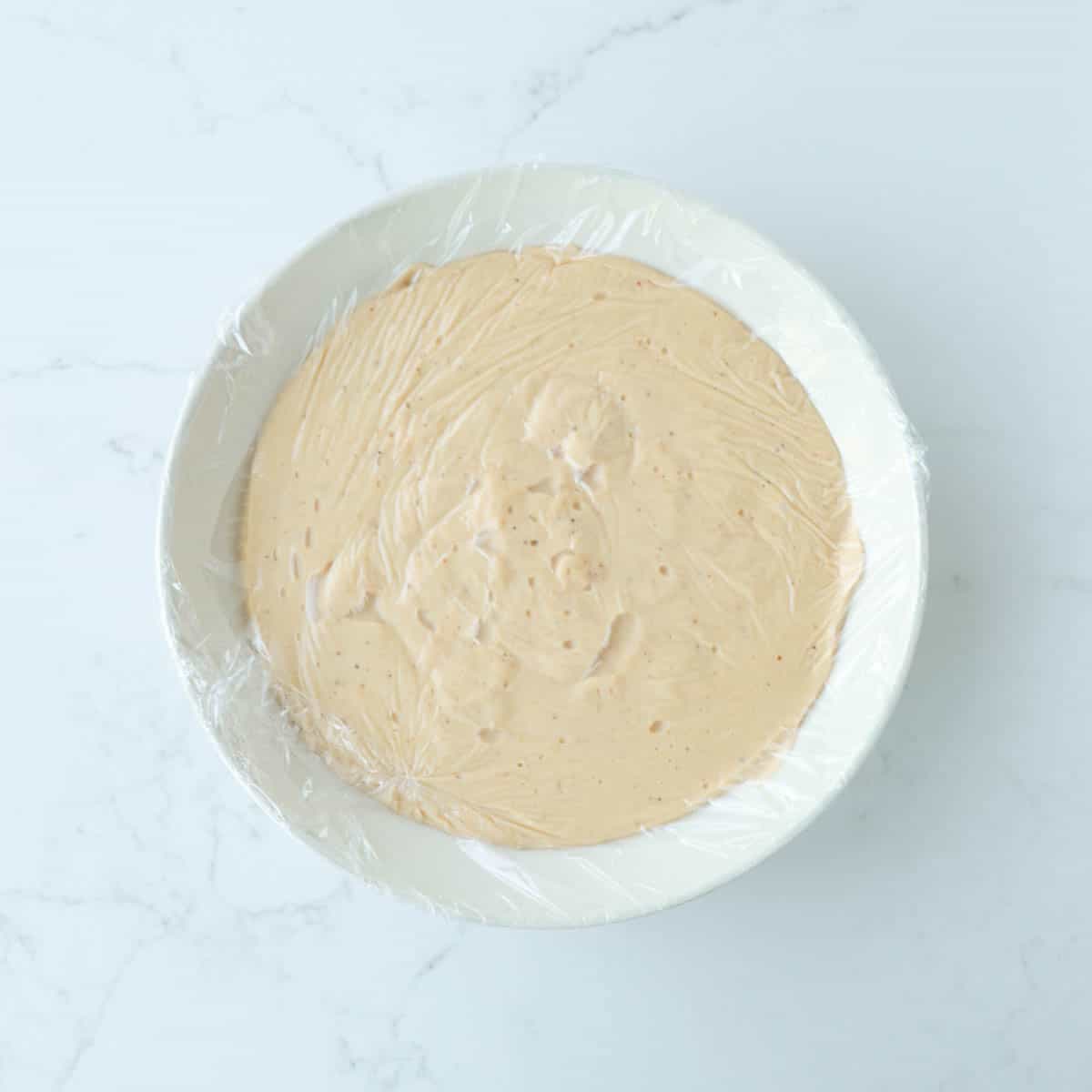 Custard in a bowl covered tightly with plastic wrap.