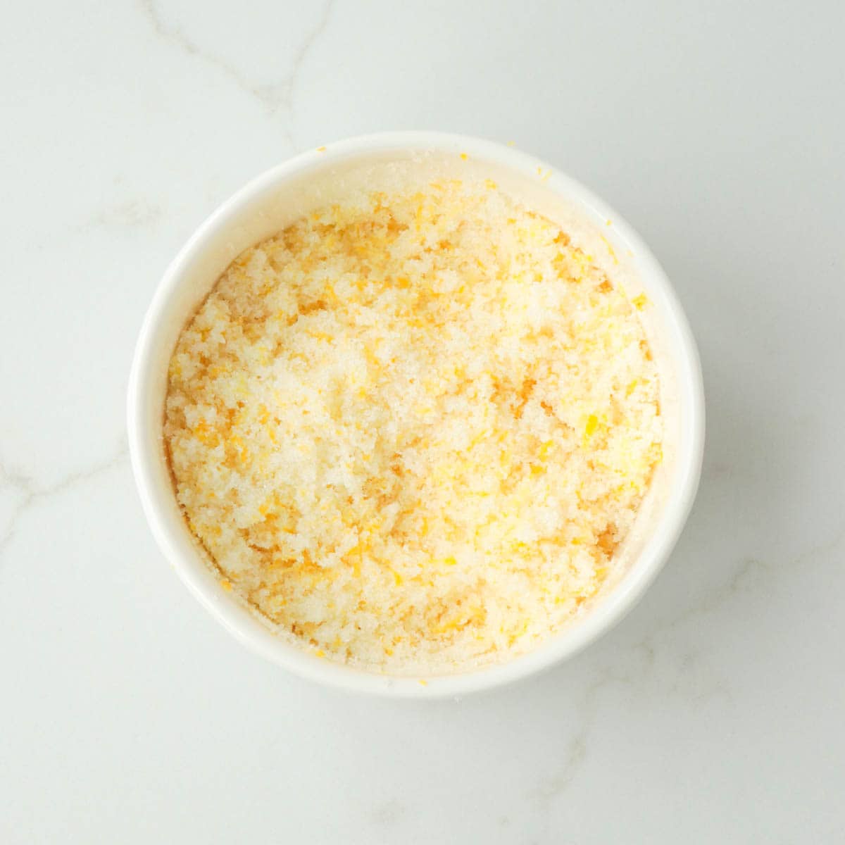 Lemon zest and sugar combined in a white bowl.