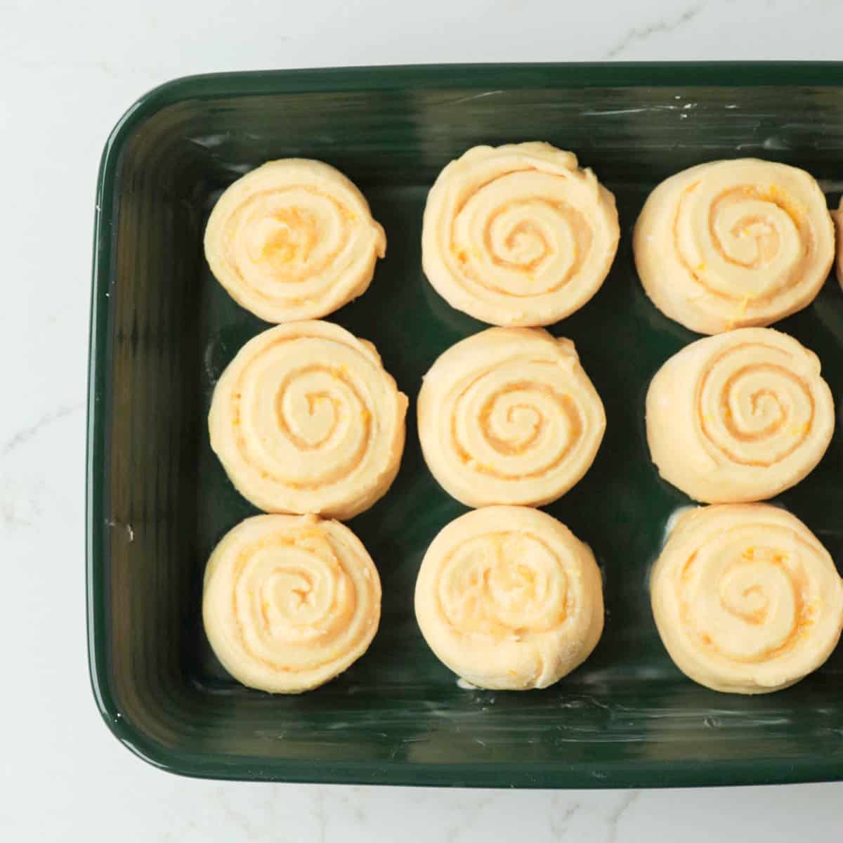 Lemon rolls in a green baking pan before rising.