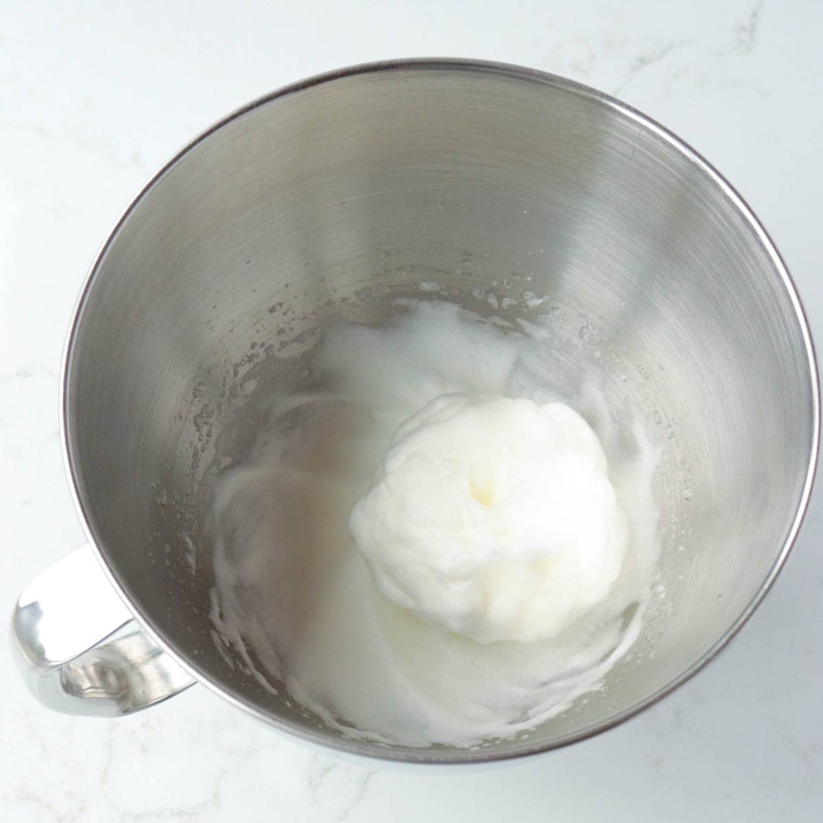 Egg whites whipped in a metal bowl.