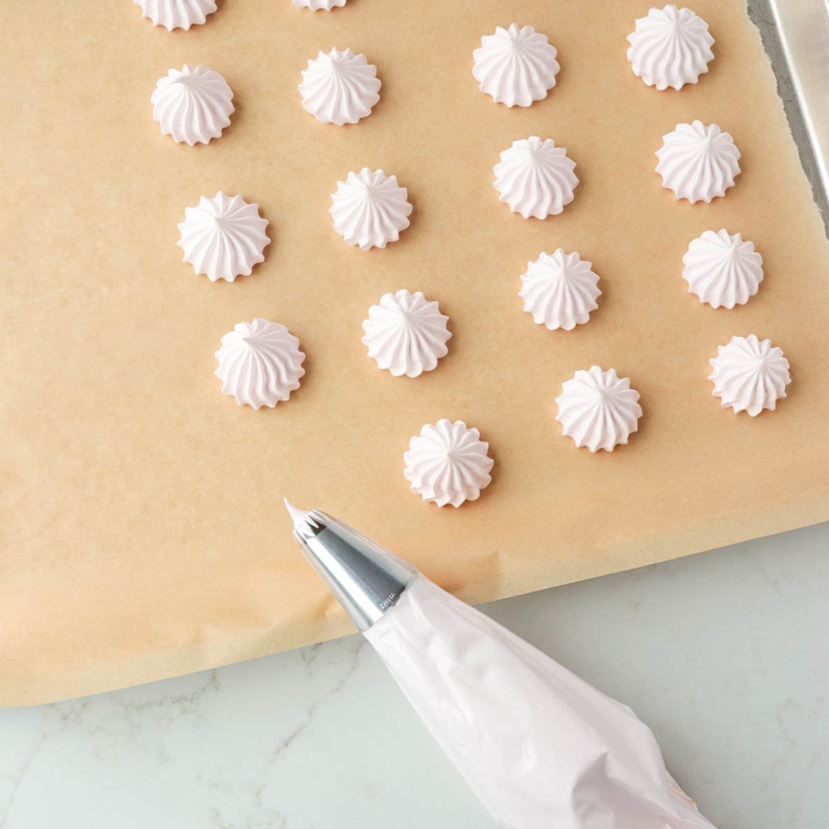 Piping meringue onto a baking sheet lined with parchment paper.