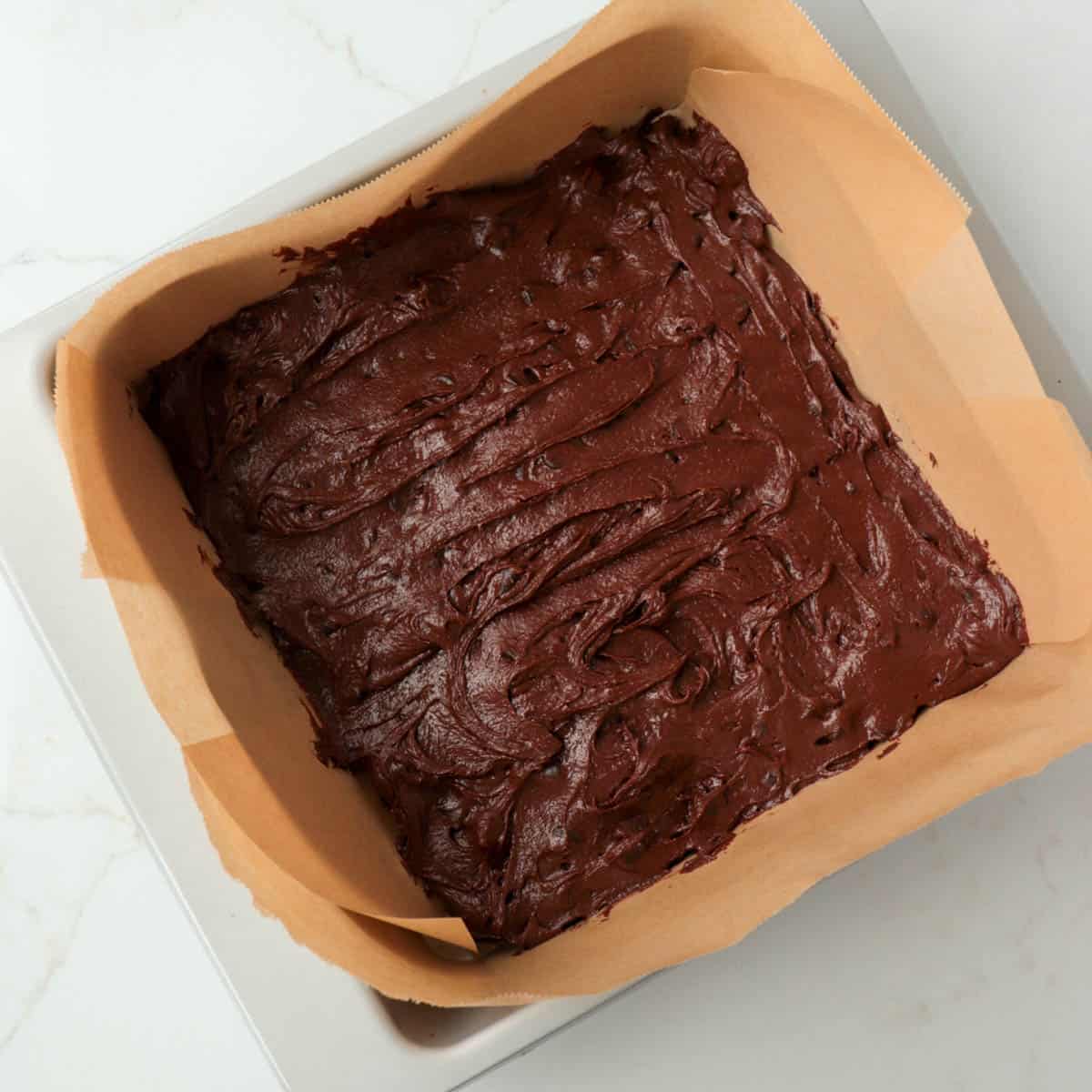 Brownie batter spread into a metal pan lined with parchment paper.
