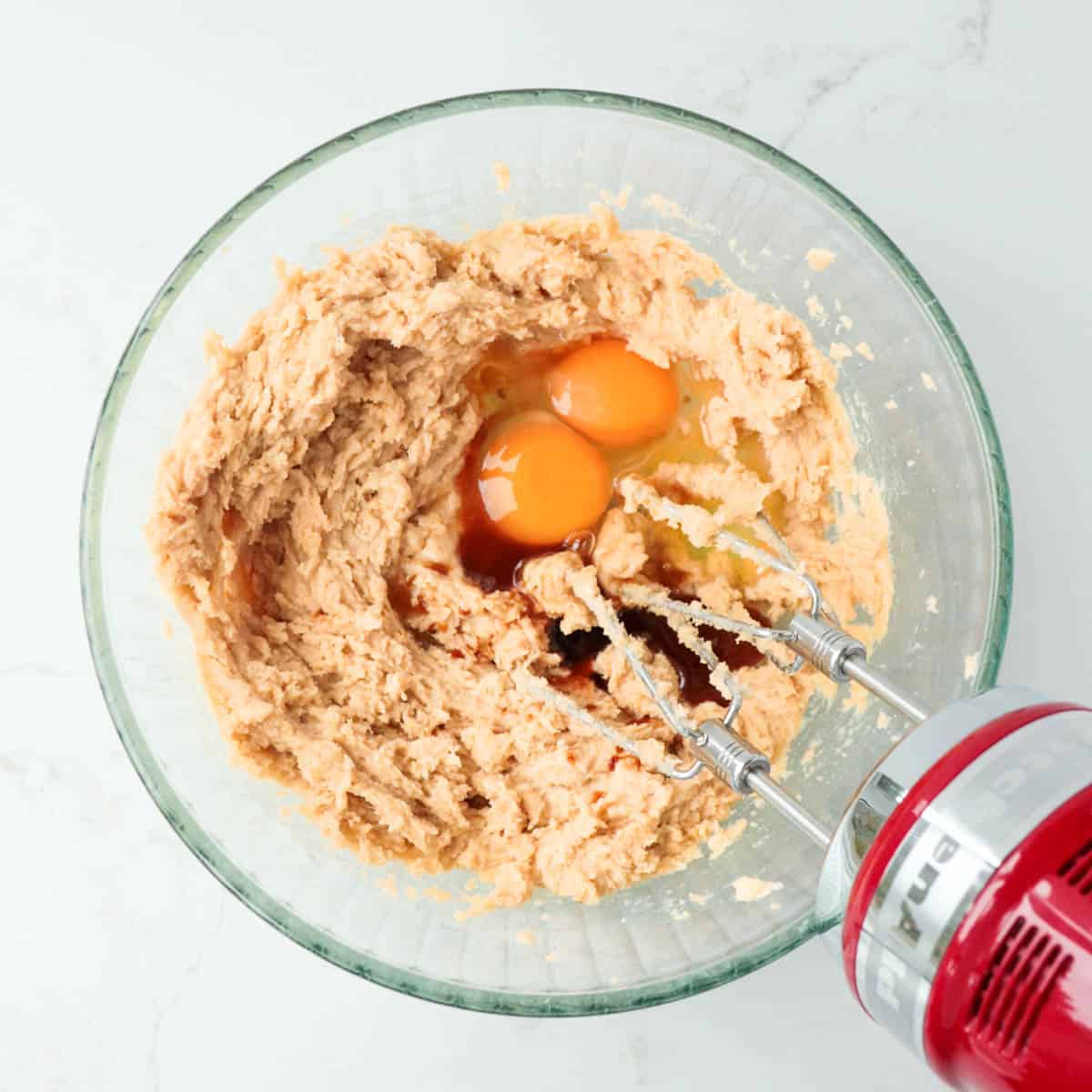 Eggs and vanilla added to combined butter and sugar in a glass mixing bowl.