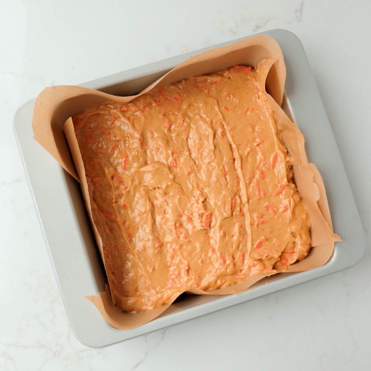 Cake batter in a metal pan lined with parchment paper.