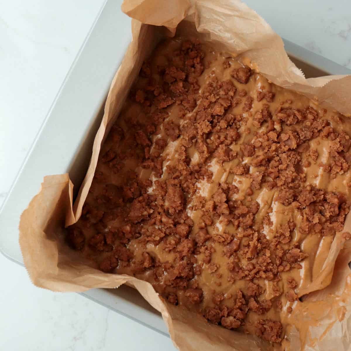 Cake batter spread into a square metal baking pan and topped with streusel.