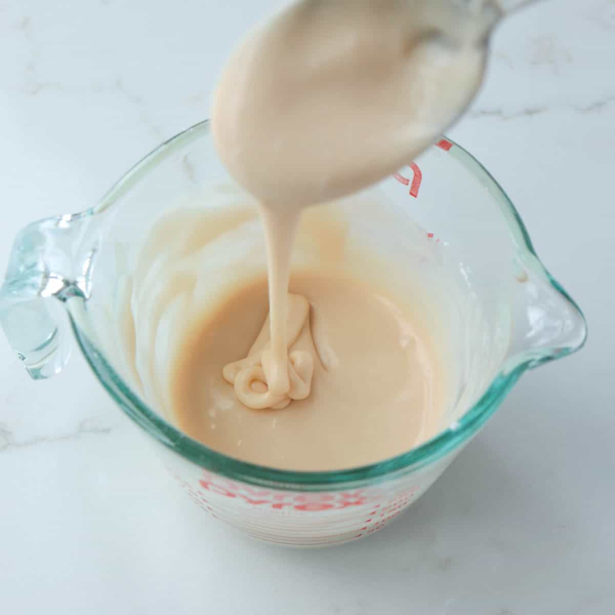 Icing dripping off of a spoon back into the bowl.