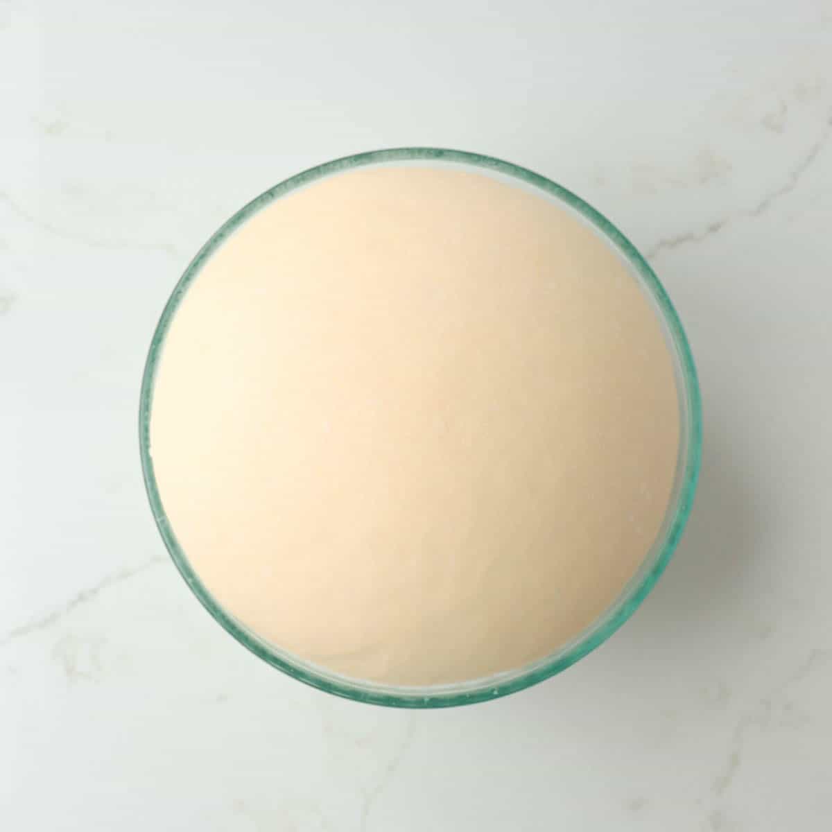 Risen dough doubled in size in a glass bowl.