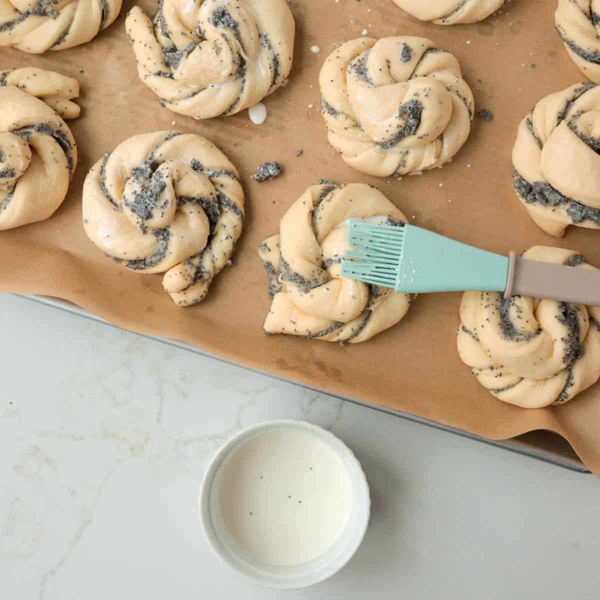 Brushing poppy seed buns with cream before baking.