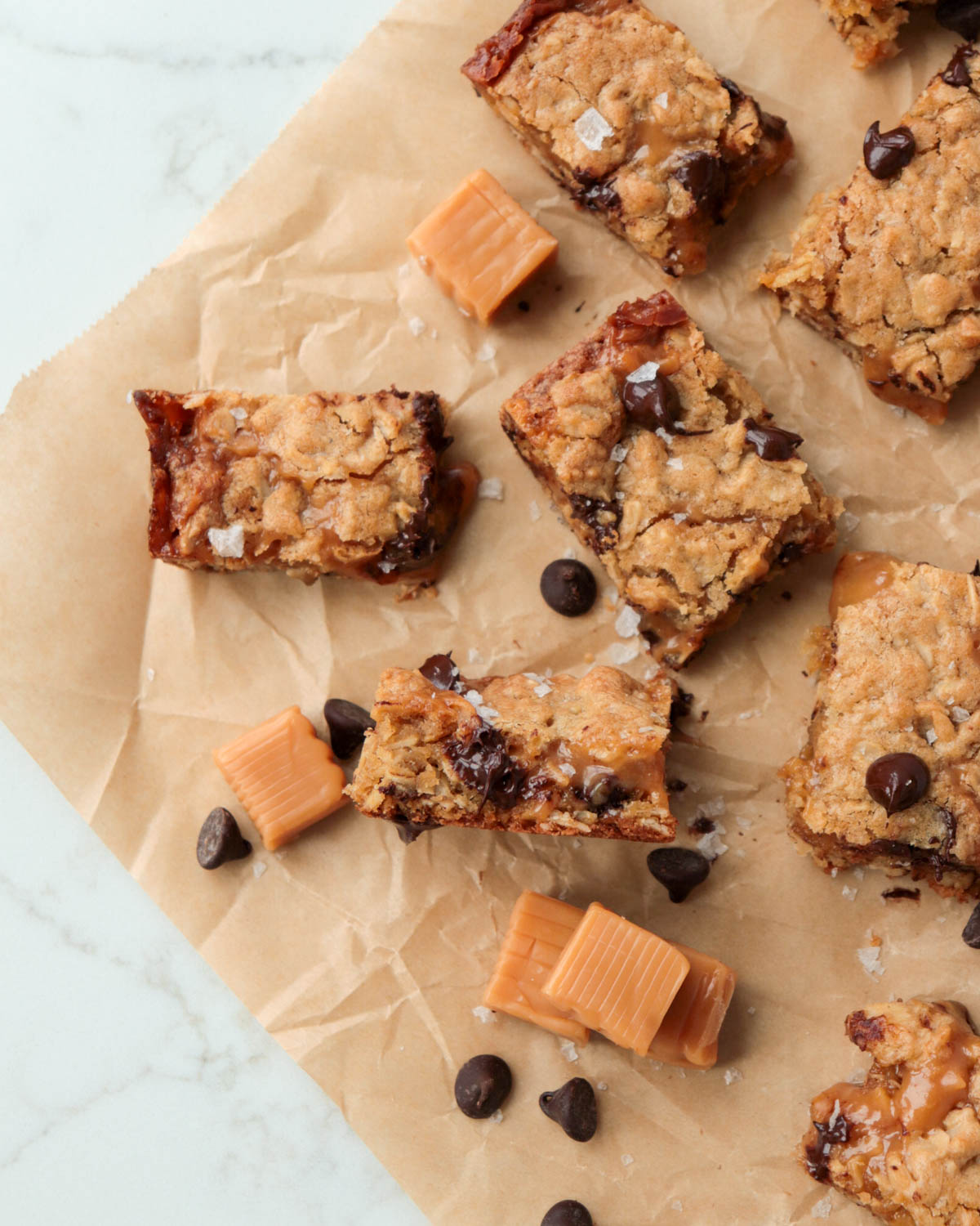 Bars on a piece of brown parchment paper with caramel squares and chocolate chips.