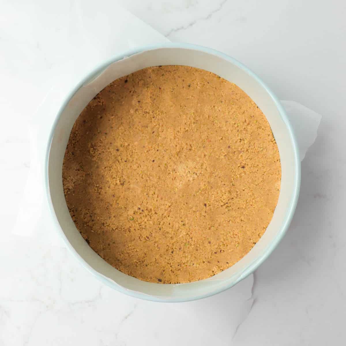 Crust pressed into the bottom of a springform pan lined with wax paper.