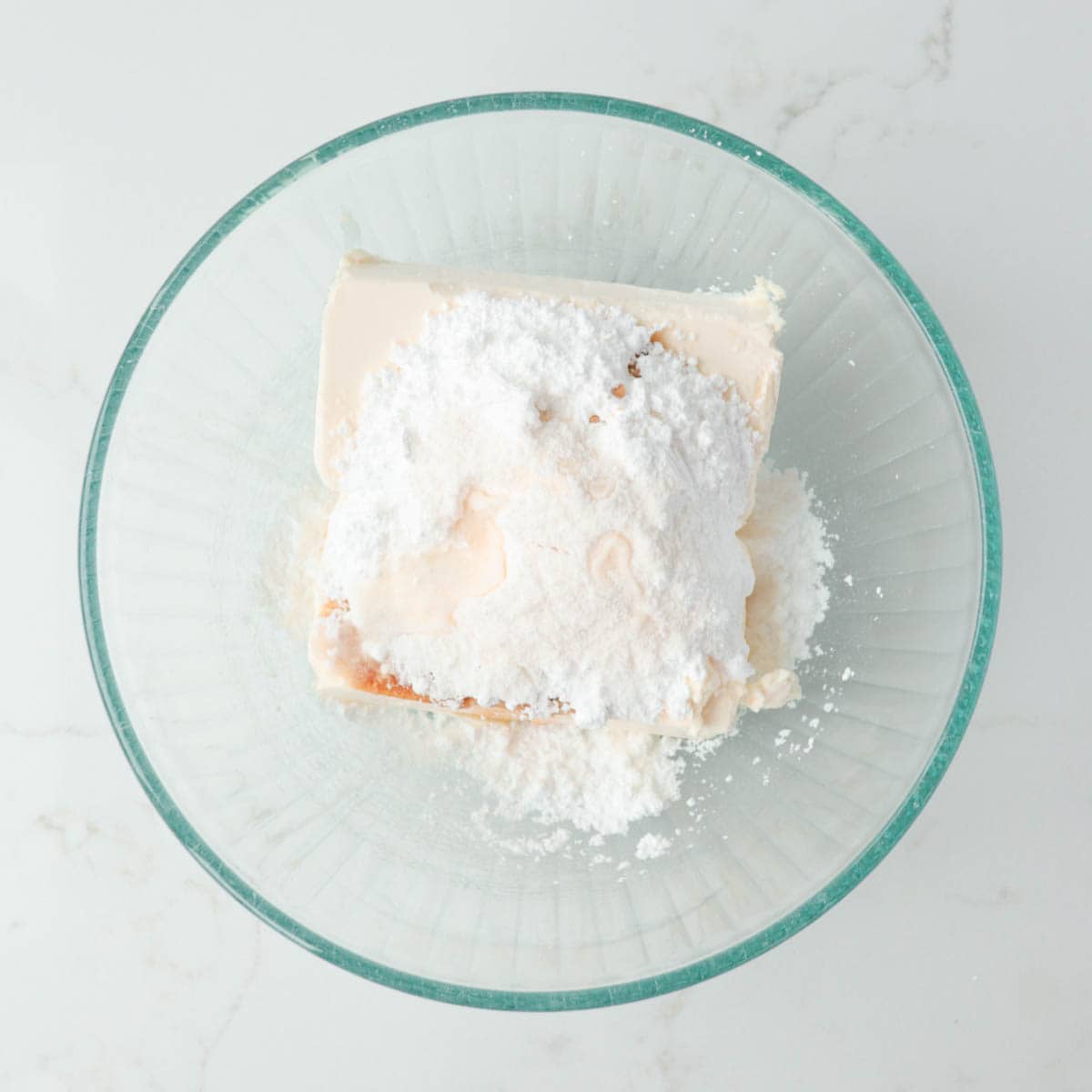 Cream cheese, extracts, and powdered sugar in a glass mixing bowl.