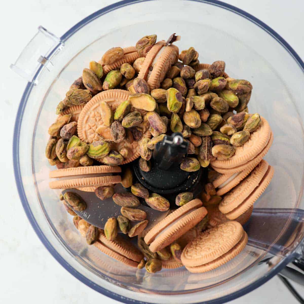 Golden Oreos and pistachios in the bowl of a food processor.