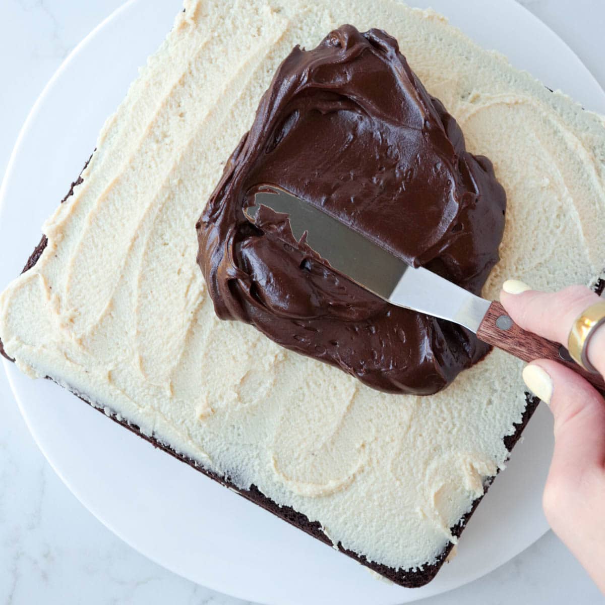 Spreading chocolate ganache on top of tahini frosting on cake.
