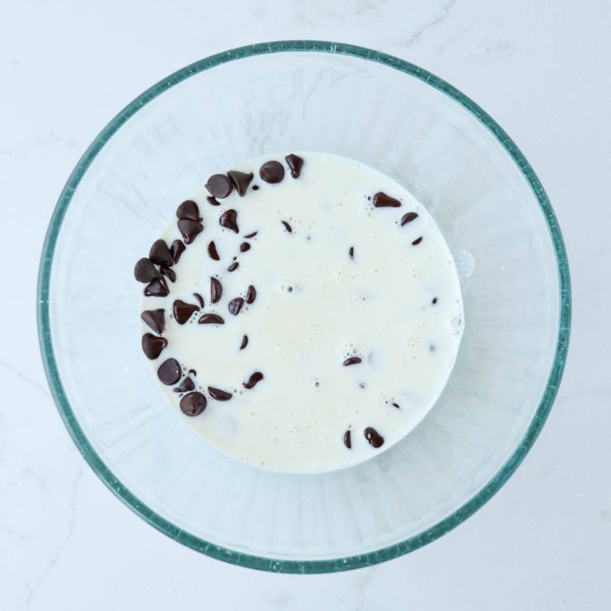 Hot cream poured over chocolate chips in a glass bowl.