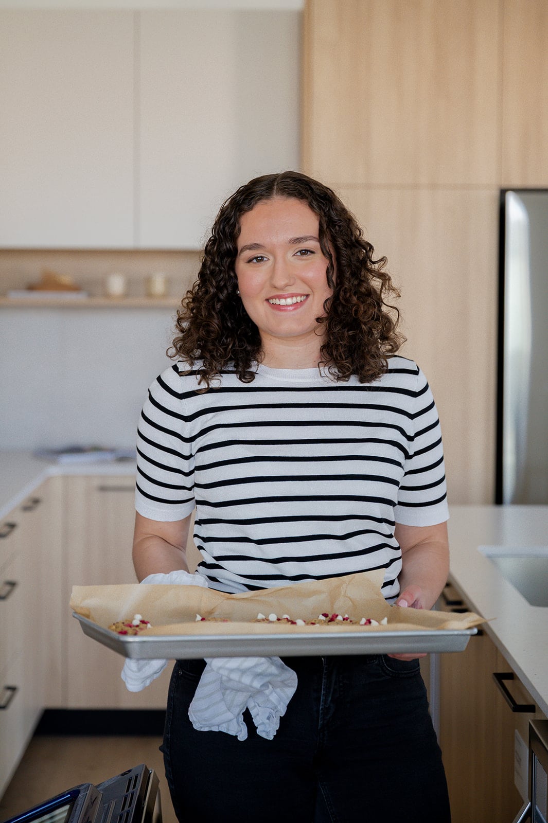 Woman wearing a black and white striped shirt holding a pan of cookies.