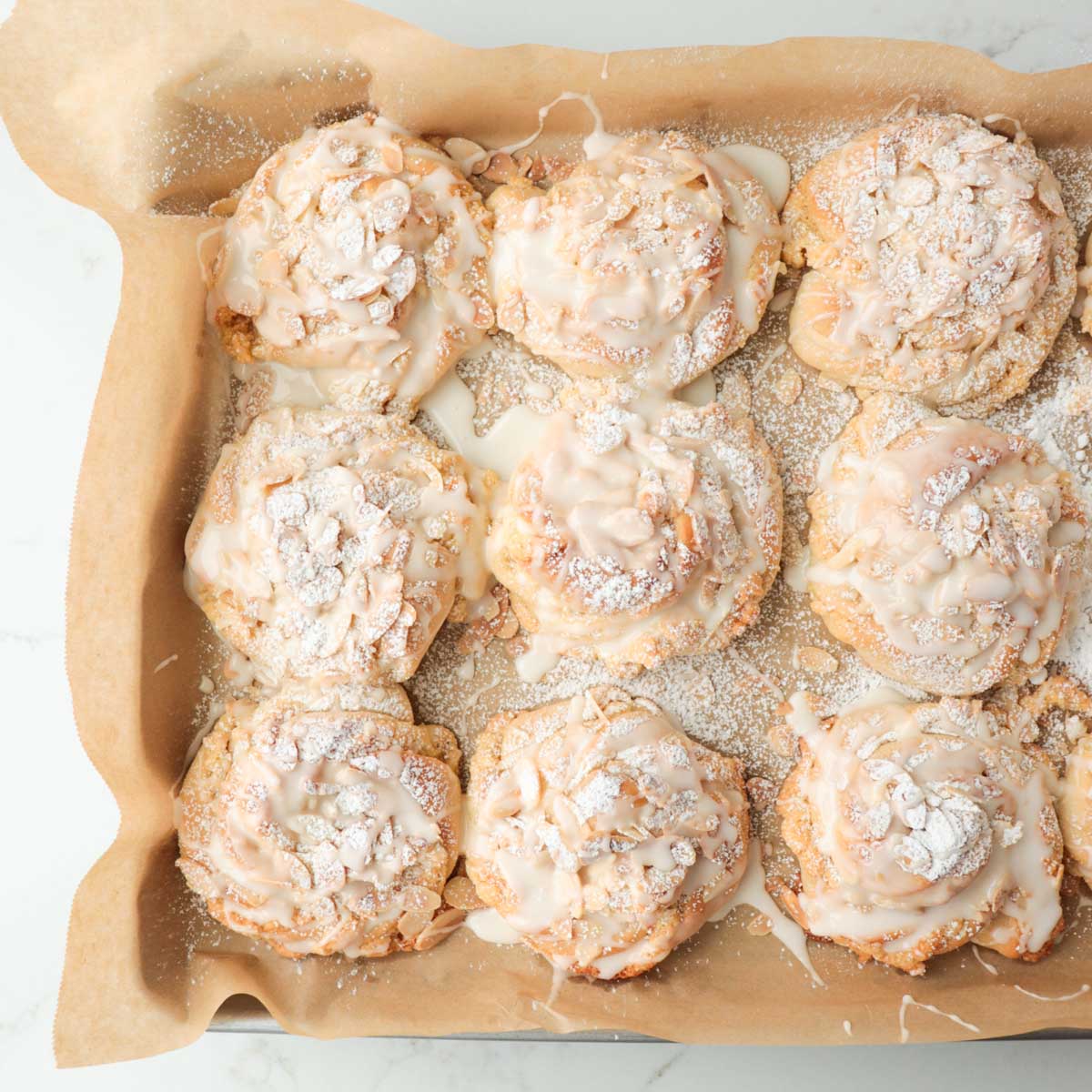 Almond buns on a pan topped with powdered sugar and icing.