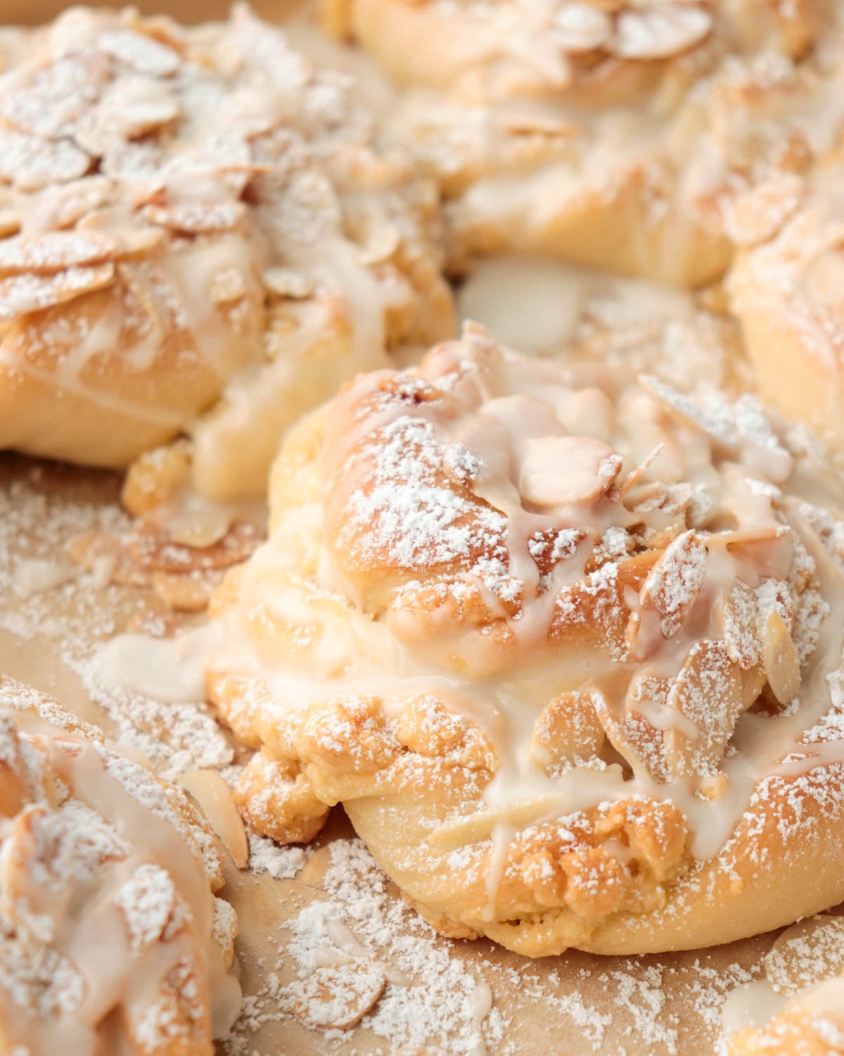 Almond bun topped with sliced almond, powdered sugar, and a drizzle of icing.