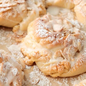 Almond bun topped with sliced almond, powdered sugar, and a drizzle of icing.